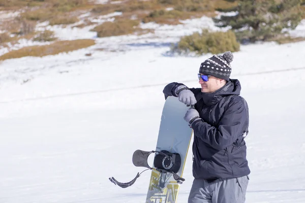 Улыбающийся человек в шляпе и солнцезащитных очках с сноубордом — стоковое фото