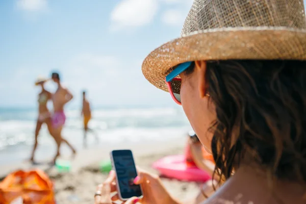 Vrouw in hat het gebruik van mobiele telefoon op strand Rechtenvrije Stockafbeeldingen