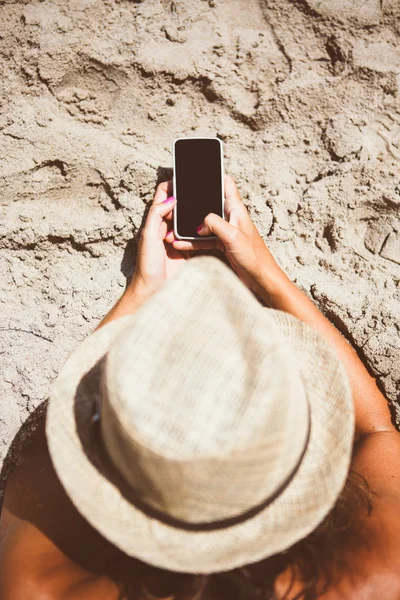 Mujer en sombrero usando teléfono móvil en la playa Imagen de stock