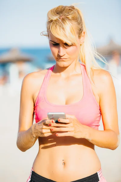 Blond idrottskvinna med mobila på stranden — Stockfoto