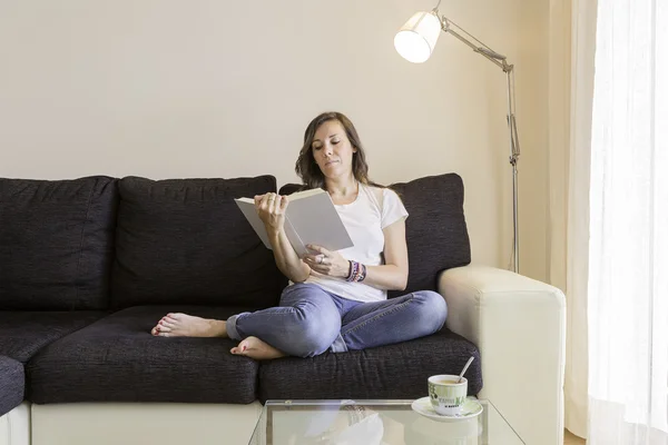 Wanita muda membaca buku di sofa — Stok Foto