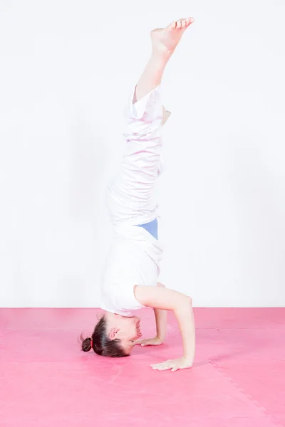 Side view of female athlete standing on head in gym-hall — Stock Photo, Image