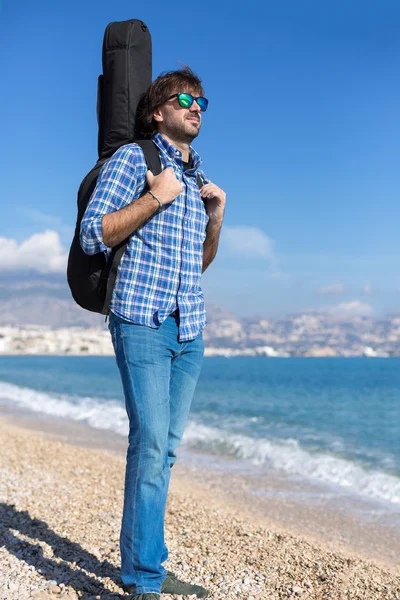 Portrait of bearded man with guitar in backpack on the beach — Stock Photo, Image