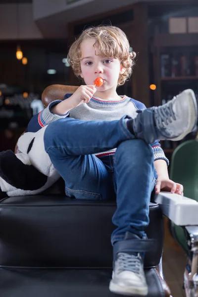 Portret chłopca siedzi w fotelu i jedzenie lizak — Zdjęcie stockowe