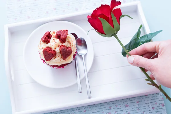 Cupcakes de San Valentín y mano sosteniendo rosa roja — Foto de Stock