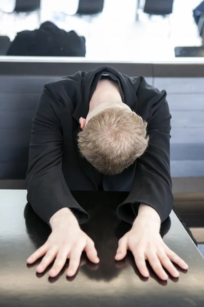 Blond boy in black coat sitting at the table put his head and ha — Stock Photo, Image