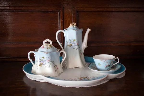 一只古董瓷盘 一只茶壶 两只杯子和一只蓝白相间的茶托 上面挂着鲜花 立在抽屉的箱子上 — 图库照片