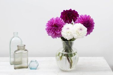 Beyaz arka planda mor ve beyaz sonbahar çiçekleri vazosu. Uzayı kopyala Hayat devam ediyor. Farklı şekillerde şişeler.