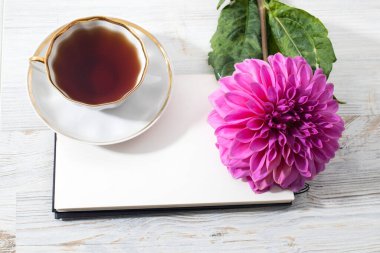 Ahşap gri, beyaz desenli masa zemininde üç mor sonbahar yıldız çiçeği. Uzayı kopyala Kart ve tasarım için çerçeve. Bir fincan çay..