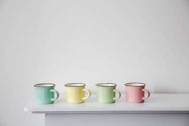 Dört küçük renkli pastel kahve fincanı beyaz bir konsolun üzerinde, arka plan duvarına karşı. Uzayı kopyala Metin için yer