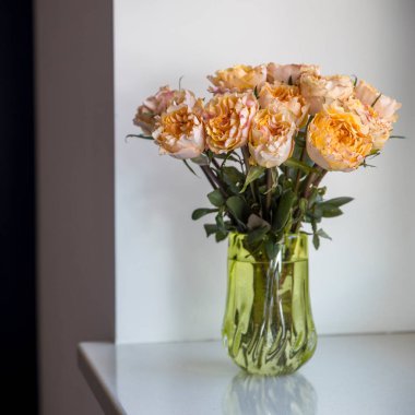 Pencere kenarındaki eski yeşil cam vazodaki turuncu güller..