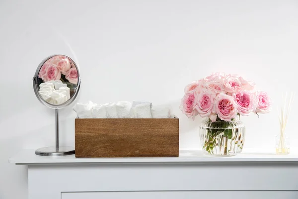 円形のガラスの透明な花瓶のローズホワイトピンクオハラは暖炉の上にあります スパのトイレにある木製の箱に白いテリーハンドタオル スペースのコピー — ストック写真