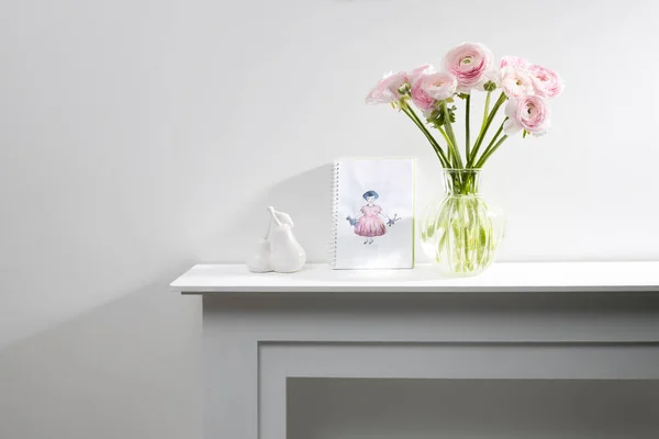 白い暖炉のコンソールのガラスの図花瓶にピンクのペルシャのバターカップの花束 2本の梨のフェイスフィギュアとインテリアとして子供の絵 スペースのコピー — ストック写真