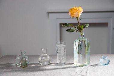 Beyaz duvarın yanındaki masada gri masa örtüsü üzerinde turuncu bir gül mumu. Boşluğu kopyala.