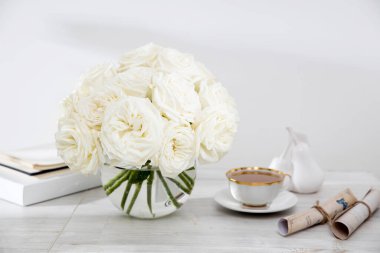 Masadaki cam vazoda bir buket beyaz gül içinde iki fincan kahve, bir çaydanlık ve bir sürahi süt. Boşluğu kopyala