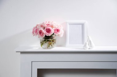 Beyaz çerçeveli yuvarlak cam vazodaki Rose White Pink O 'hara fotoğraf ve paketlenmiş hediyeler şöminenin üzerinde. Boşluğu kopyala
