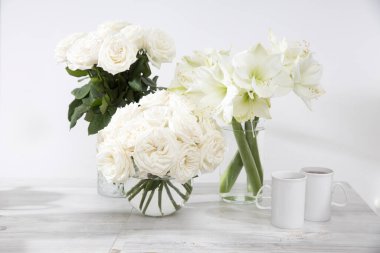 Beyaz güller, zambak, yuvarlak vazolarda, masada iki fincan kahve ile mutfak dekorasyonu için. Boşluğu kopyala