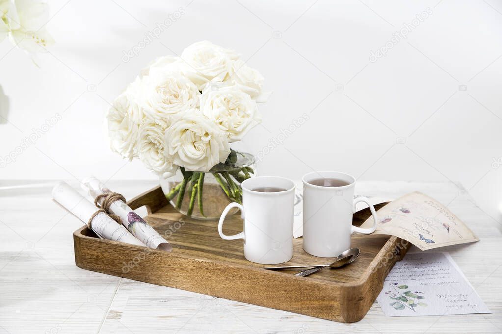 Moscow, Russia - 25 December 2020, A bouquet of white roses in a glass vase on a tray with two cups of coffee, a kettle, and a milk jug. Copy space