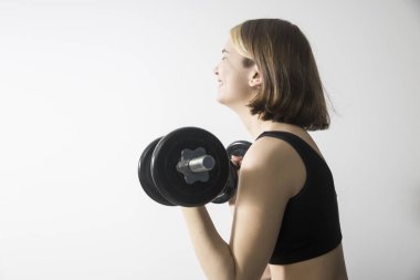 Kısa gri bluzlu, kısa saçlı, kısa saçlı, kısa saçlı, kısa saçlı, gülümseyen 19 yaşında bir kız, beyaz arka planda bir halter tutuyor. Spor ve sağlık konsepti.