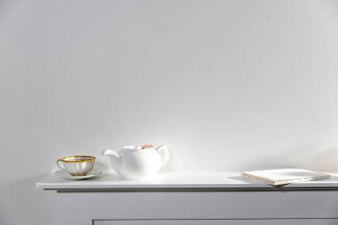 Beyaz üstüne beyaz. Bir fincan çay, bir çaydanlık ve suni şöminenin beyaz panelinde duran bir defter. Boş boşluk.