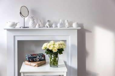 Beyaz şömine konsolunda cam vazoda duran beyaz güller. İç dekorasyon için bir melek figürü olarak. Uzayı kopyala Gül Beyaz Pembe O 'hara.