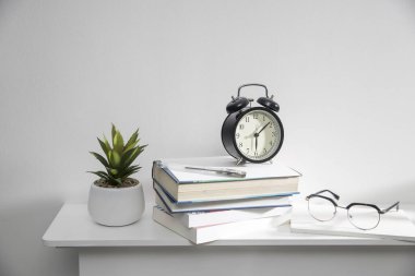 Bir yığın kitap, seramik kapta yapay sulu bir bitki, bardaklar, defterli metal bir sepet, beyaz bir masa yüzeyinde bir kalem. Konsept: Ofis evde. Çevrim içi eğitim.