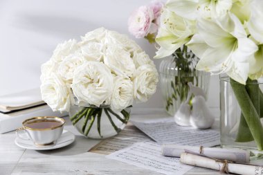 Londra, İngiltere - 20 Mart 2021, bir fincan çay ve bir kitapla birlikte yuvarlak cam bir vazoda bir buket beyaz gül. Boşluğu kopyala.