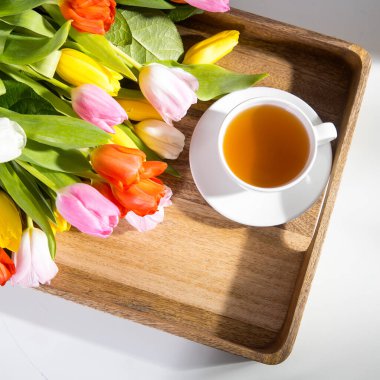 Masadaki ahşap tepside bir buket çok renkli lale ve bir fincan çay var.