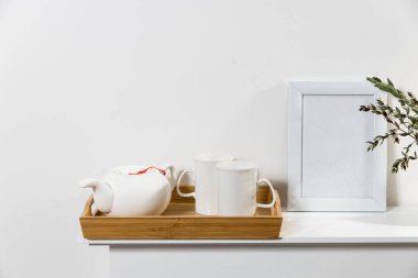 Beyaz şekilli bir toprak vazoda okaliptüsün kuru dalı. Masadaki ahşap tepside çay için iki büyük bardak çay. İskandinav tarzı. Uzayı kopyala Boş alanı olan beyaz fotoğraf çerçevesi