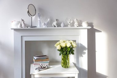 Beyaz şömine konsolunda cam vazoda duran beyaz güller. İç dekorasyon için bir melek figürü olarak. Uzayı kopyala Gül Beyaz Pembe O 'hara.