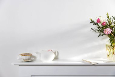 Beyaz üstüne beyaz. Bir fincan çay, bir çaydanlık ve suni şöminenin beyaz panelinde duran bir defter. Boş boşluk.