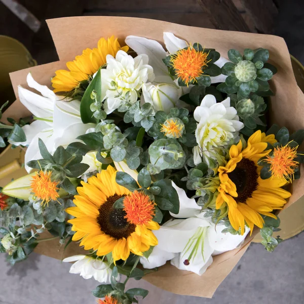 Wedding bouquet of sunflowers, white chrysanthemum, lilies, eucalyptus and marigold wrapped in craft paper in a bucket for sale