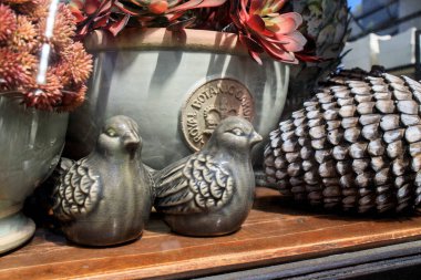 Teneke bir havuzda gri seramik kuşlar, bahçe bitkilerinin arka planında duran taş enginarlar. Güneşli bir gün. Pazar.