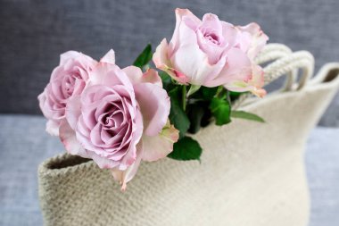 Üç soluk mor gül beyaz örgülü bir ip plaj çantasından görülebilir. Denizde bir araya gelme zamanı.