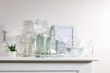 Farklı şekillerde, fotoğraf çerçeveli bir su şişesi ve şifoniyerin üzerinde yapay sulu bir tencere var. Boşluğu kopyala