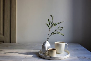 Minimalist İskandinav tarzı. Masadaki tepside iki kişilik iki fincan farklı boyutta kahve. Kuru okaliptüs dalıyla kaplanmış vazo.