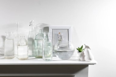 Farklı şekillerde, fotoğraf çerçeveli bir su şişesi ve şifoniyerin üzerinde yapay sulu bir tencere var. Boşluğu kopyala