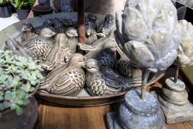 Teneke bir havuzda gri seramik kuşlar, bahçe bitkilerinin arka planında duran taş enginarlar. Güneşli bir gün