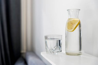 Ferahlatıcı bir bardak su, içinde bir dilim limon olan bir şişe yaz sıcağında şifoniyerin üstünde.