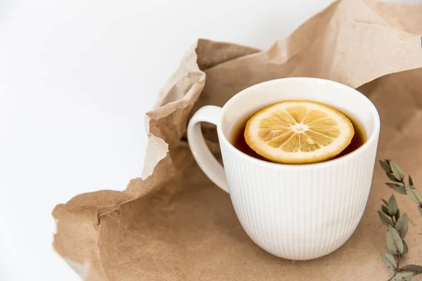 茶とレモンの白い段ボールカップは 木製のテーブルの上に茶色のクラフト紙にあります — ストック写真