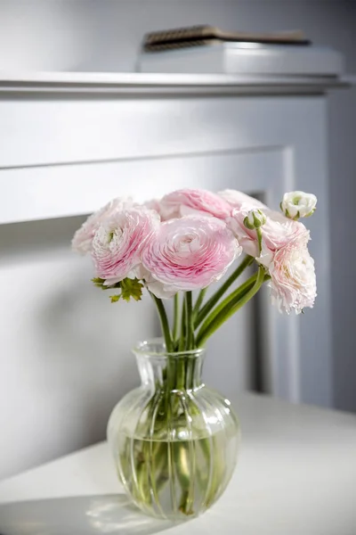 暖炉の後ろのテーブルの上のガラスの花瓶の淡いピンクのペルシャのバターカップの花束 — ストック写真