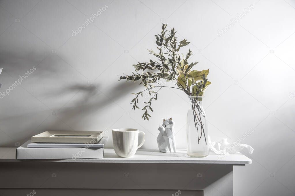 A vase with dry eucalyptus, pieces of paper, a figurine with a fox and a cup of coffee. Scandinavian style.