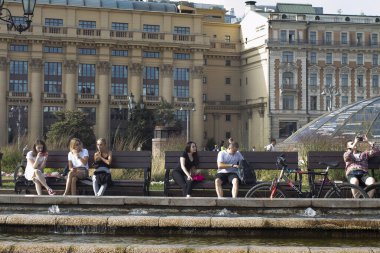 Moskova, Rusya - 21 Haziran 2021, Manezhnaya Meydanı 'nda Ulusal Otel' in önündeki banklarda oturan kadınlar ve erkekler.