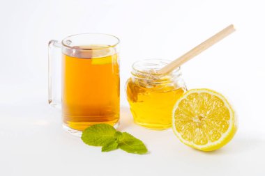Beyaz zemin üzerinde bal, limon ve nane ile bir bardak çay..