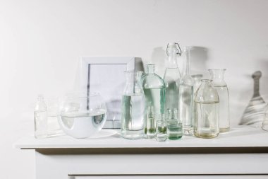 Farklı şekillerde, fotoğraf çerçeveli bir su şişesi ve şifoniyerin üzerinde yapay sulu bir tencere var. Boşluğu kopyala