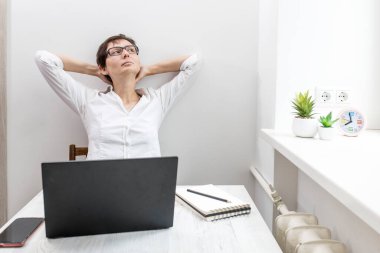 Orta yaşlı, kısa saçlı, gözlüklü esmer bir kadın pencerenin yanındaki dizüstü bilgisayarda çalışıyor. Elleri başının arkasında olan ofis çalışanı duvara yaslanmış, dinleniyordu.