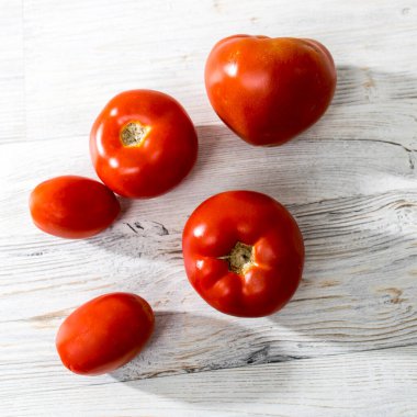 Bej ahşap bir masada farklı türde taze domates bulunur.