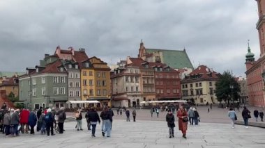 Varşova, Polonya, 8 Ekim 2025. Bir grup turist Castle Square 'deki Eski Şehir' de yürüyor. Kraliyet Kalesi ve savunma duvarı bulutlu ve güneşli dramatik bir gökyüzüne karşı yükseliyor..