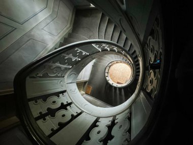 Koyu halı ve süslü korkulukları olan eski bir sarmal merdivenden aşağı bak.