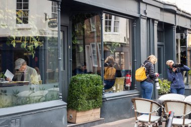 Brighton, İngiltere, 2 Mayıs 2025. İki kadın, bir sokak kafesinin önünde, içeride kitap okuyan bir adamla fotoğraf çekiyor.